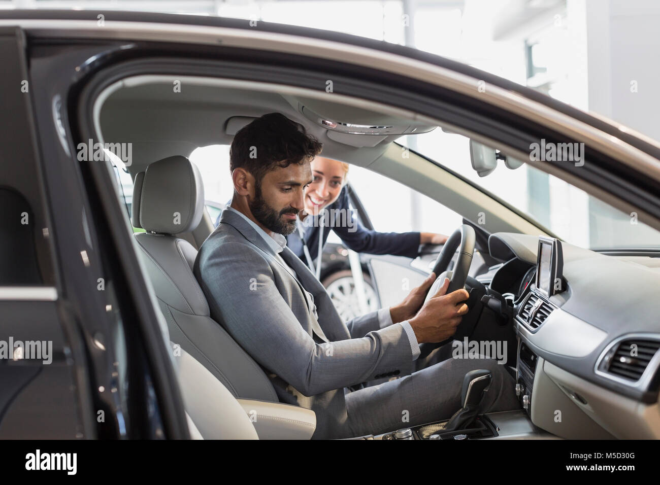 Car saleswoman and male customer in driver’s seat of new car in car dealership showroom Stock Photo