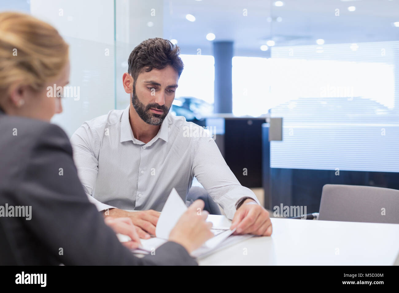 Car saleswoman explaining financial contract paperwork to male customer in car dealership office Stock Photo