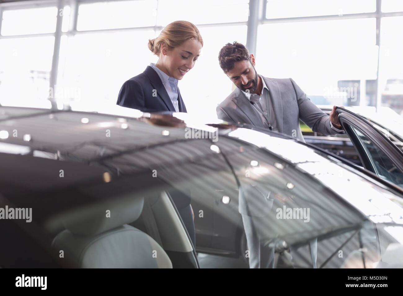 Car salesman showing new car to female customer in car dealership showroom Stock Photo