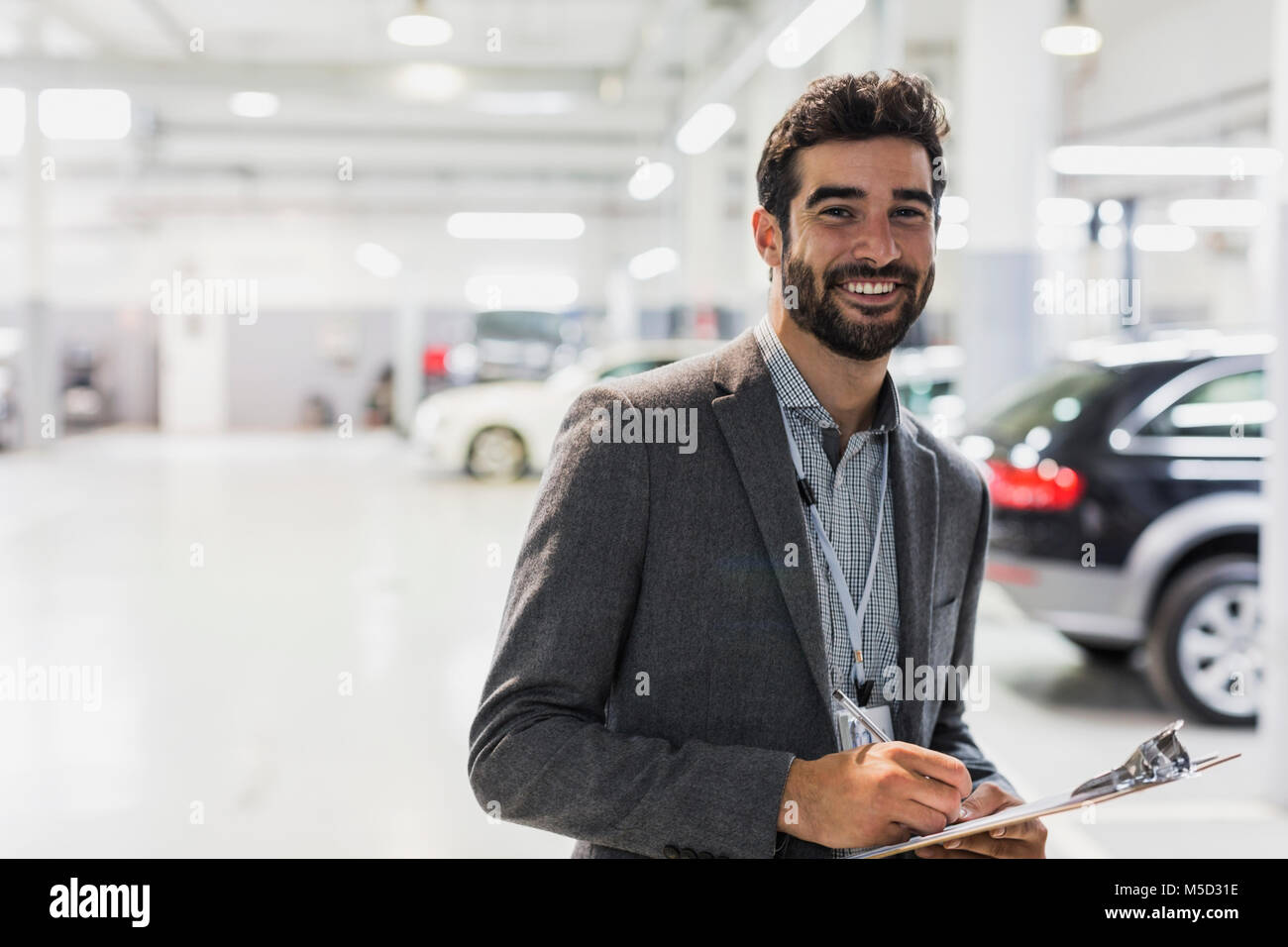 Portrait smiling, confident car salesman with clipboard in car dealership auto repair shop Stock Photo