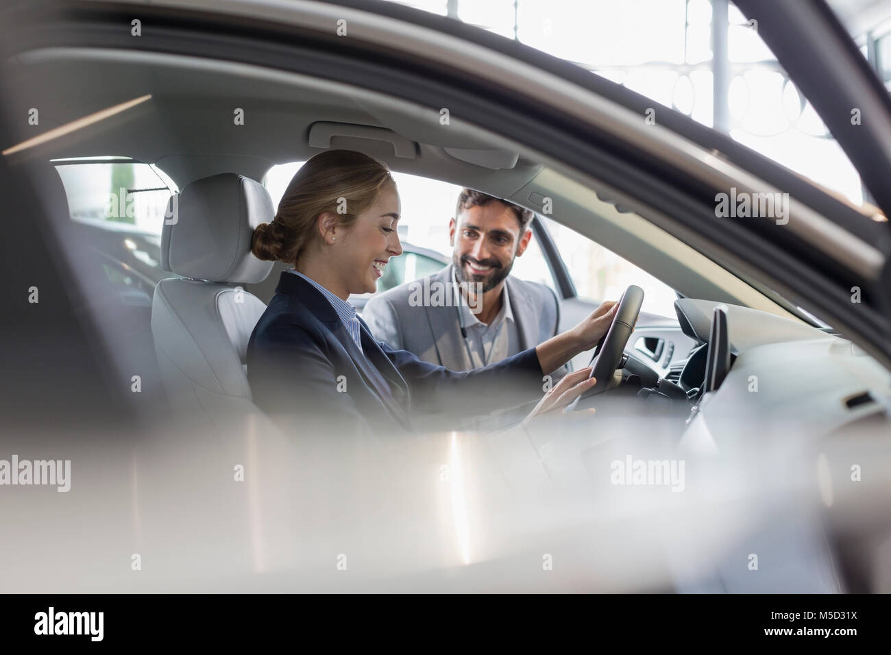 Car salesman showing new car to female customer in driver’s seat in car dealership showroom Stock Photo