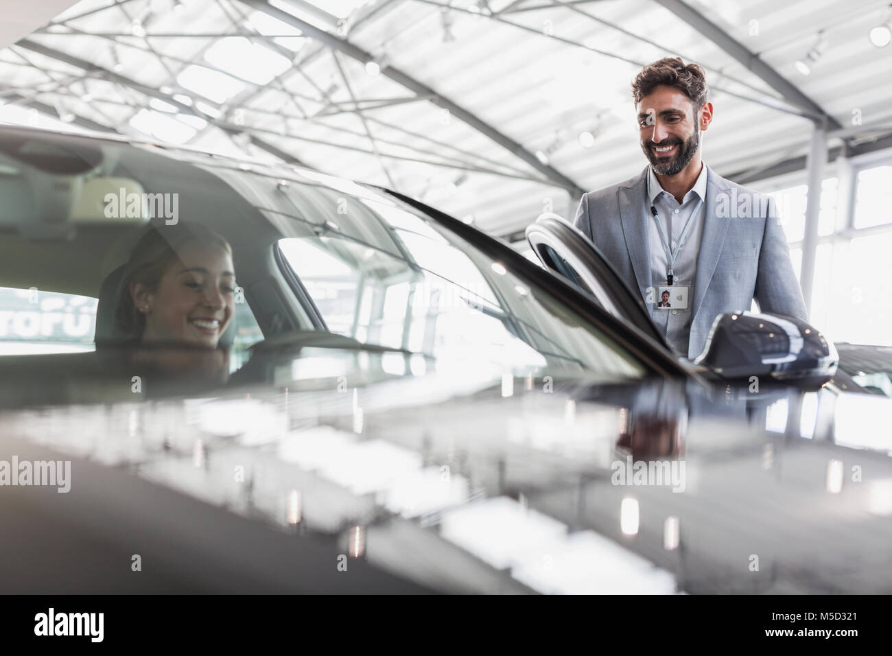 Smiling car salesman and female customer in driver’s seat of new car in car dealership showroom Stock Photo