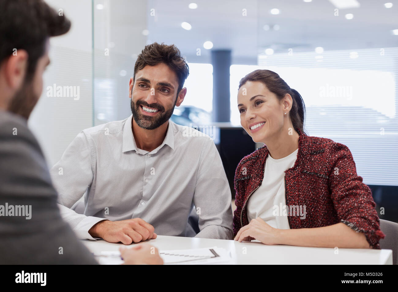 Smiling couple customers talking to car salesman in car dealership office Stock Photo