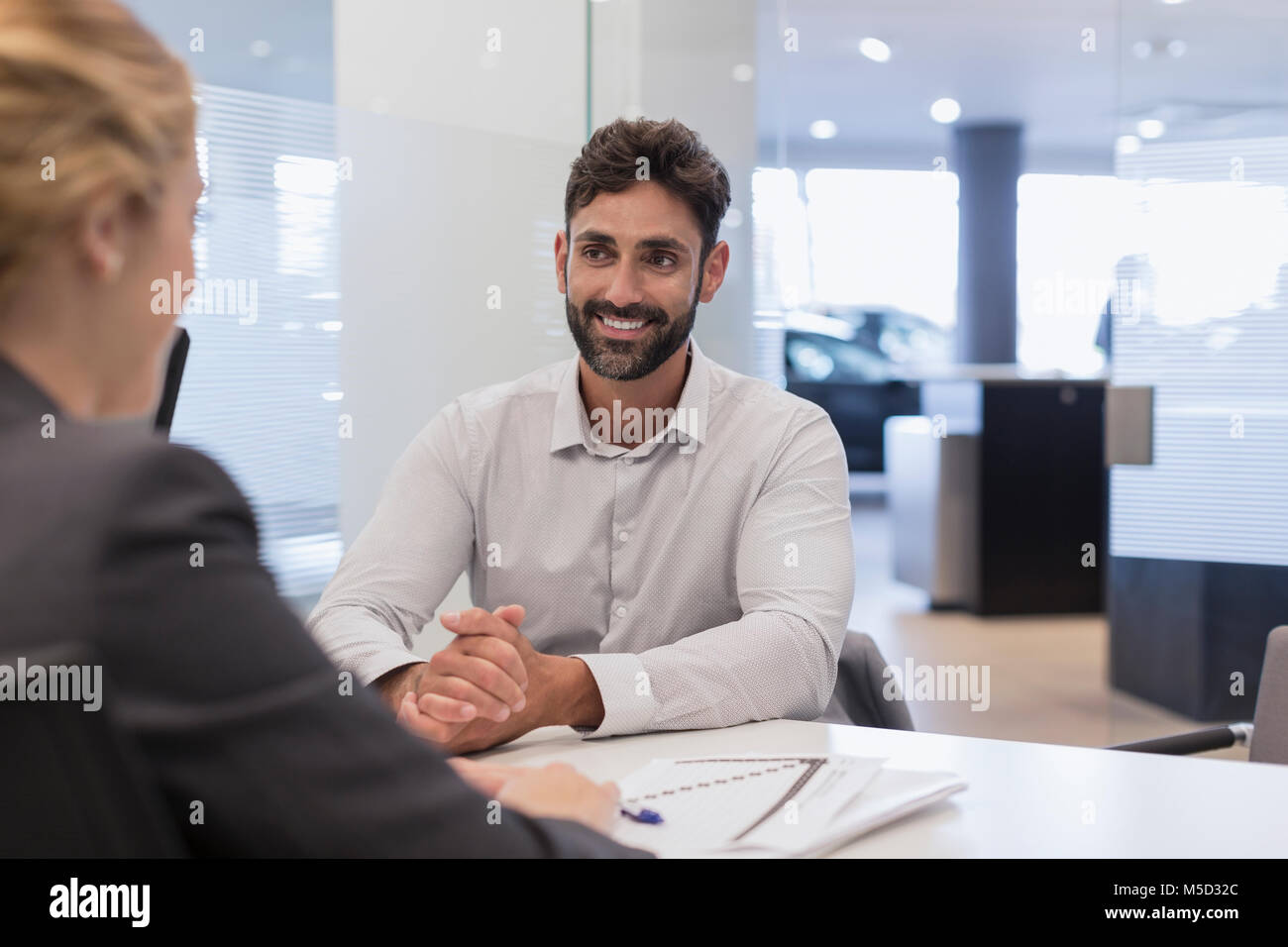 Smiling male customer listening to car saleswoman in car dealership office Stock Photo
