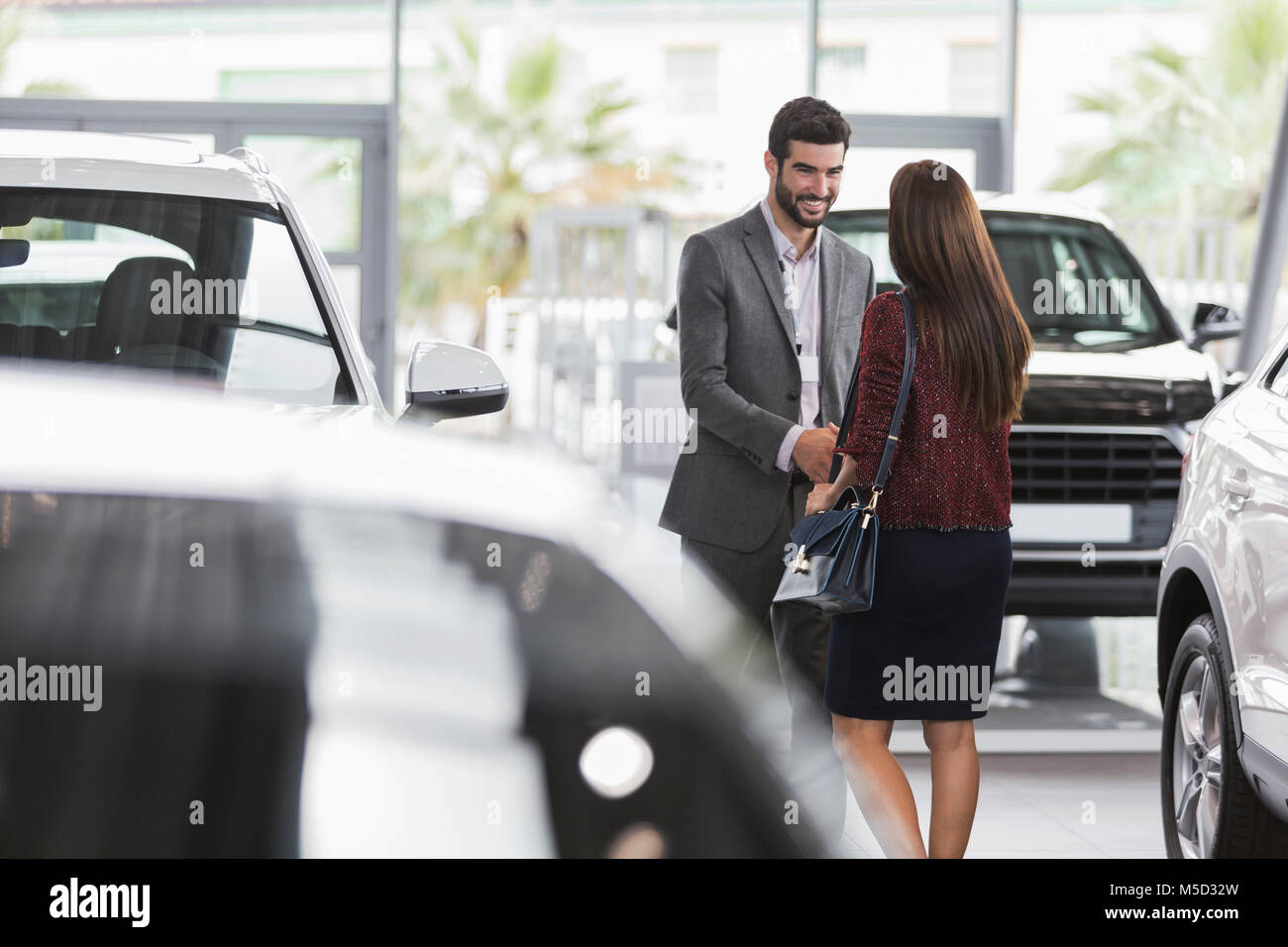 Car salesman greeting, shaking hands with female customer in car dealership showroom Stock Photo