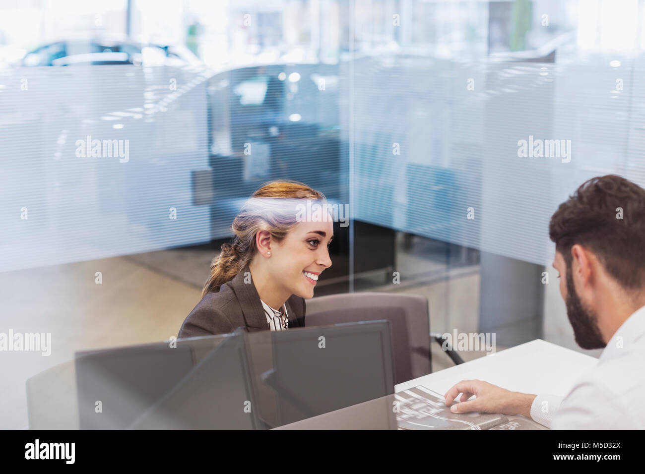 Smiling car saleswoman talking to male customer in car dealership office Stock Photo