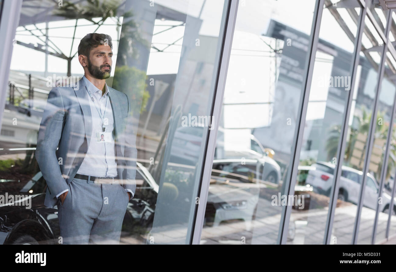 Serious, pensive car salesman looking out car dealership showroom window Stock Photo