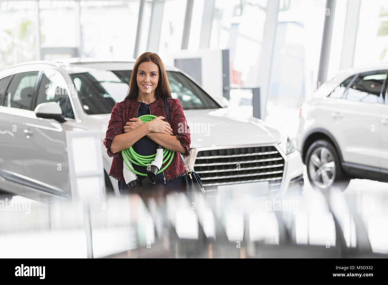 Portrait smiling female customer holding hybrid charging cable in car dealership showroom Stock Photo