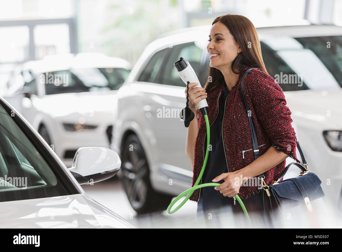 Smiling female customer carrying hybrid charging cable in car dealership showroom Stock Photo