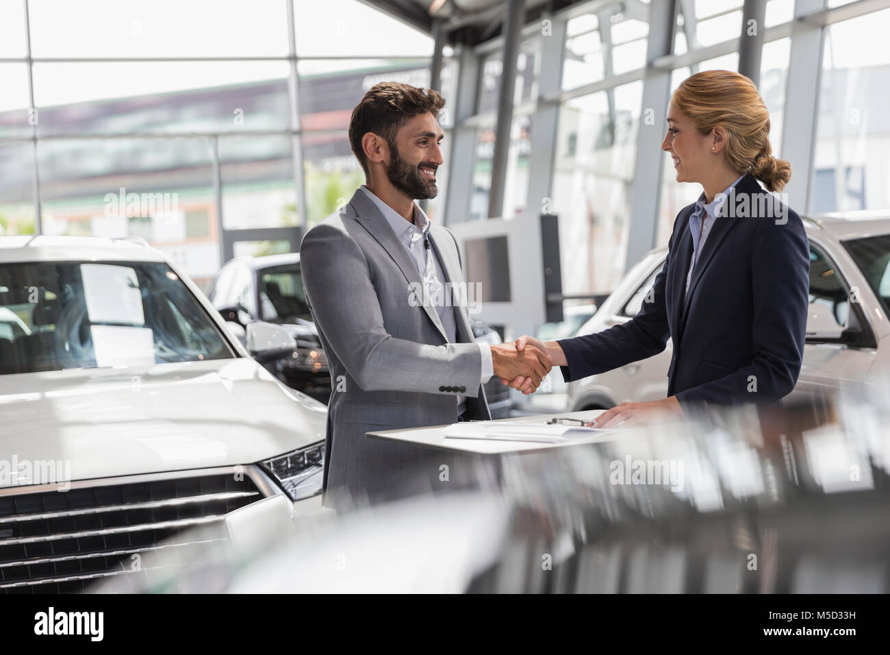Car saleswoman and male customer handshaking in car dealership showroom Stock Photo