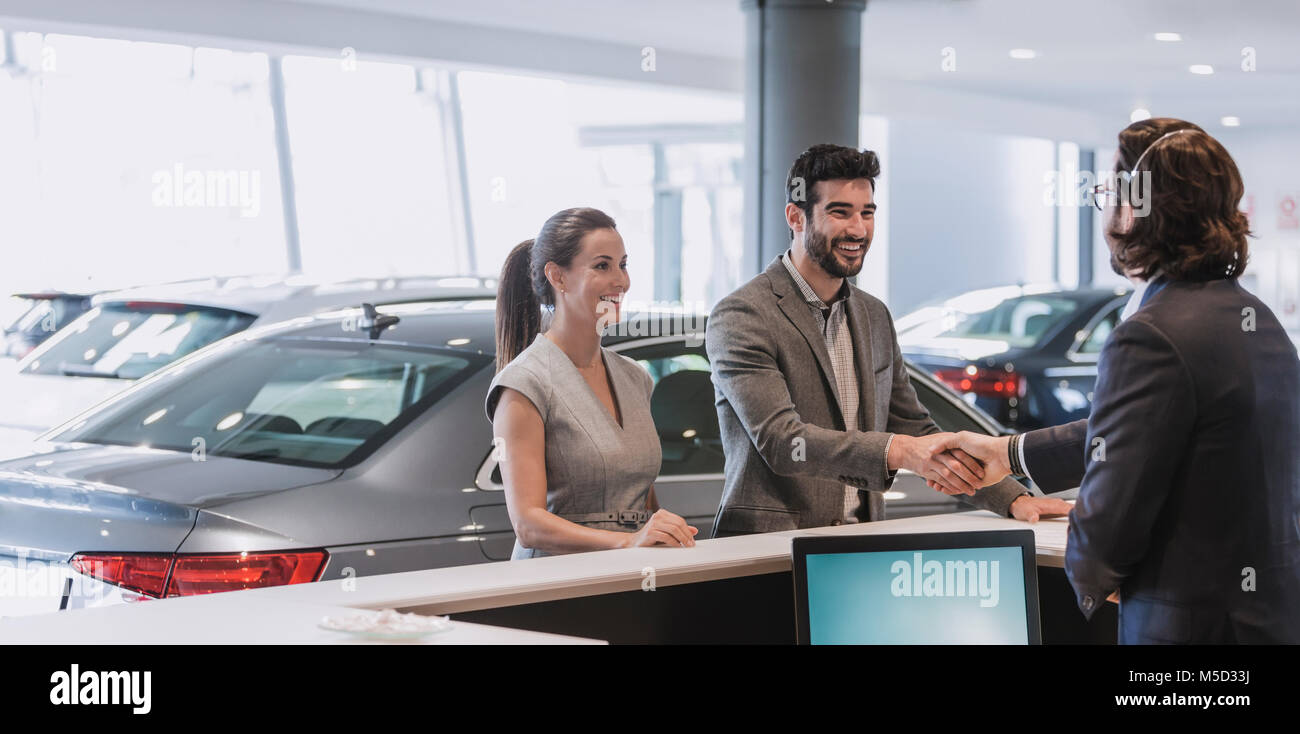 Couple arriving, greeting receptionist and handshaking at car dealership showroom Stock Photo
