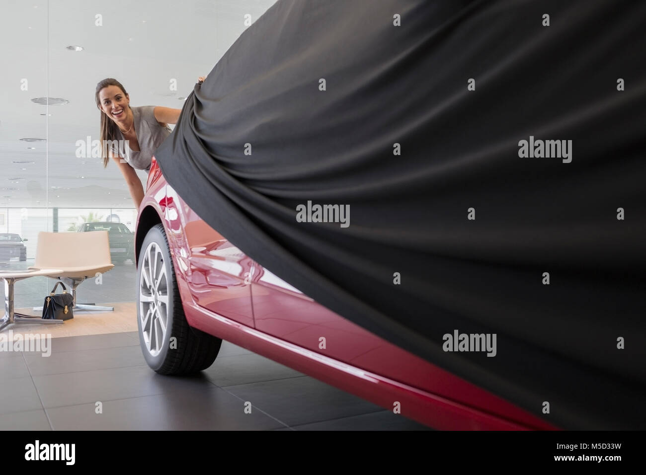 Female customer removing cover from new car in car dealership showroom Stock Photo