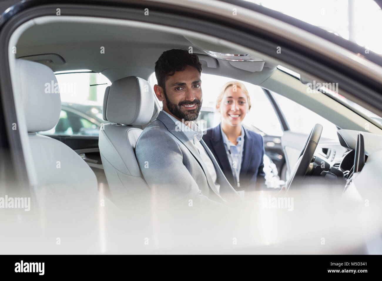 Portrait smiling, confident car saleswoman and male customer in driver’s set of new car in car dealership Stock Photo