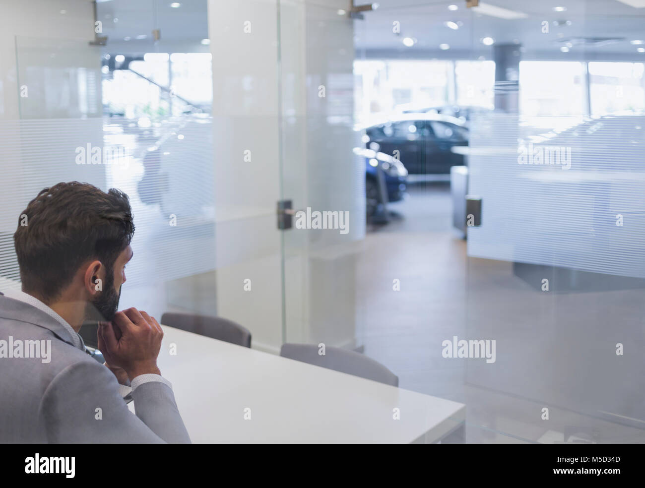 Pensive car salesman sitting in anticipation in car dealership office Stock Photo