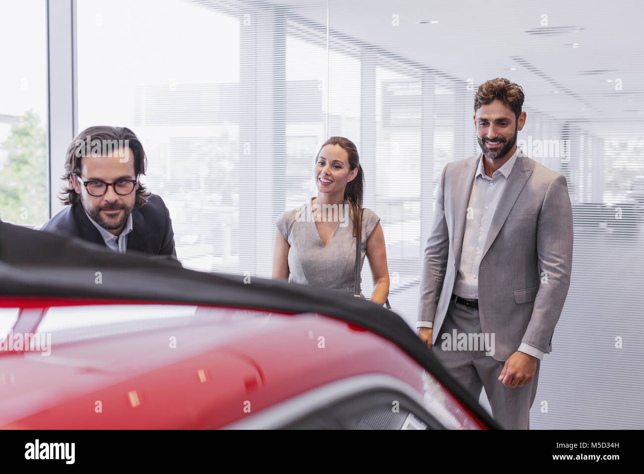 Car salesman showing new car to couple customers in car dealership showroom Stock Photo