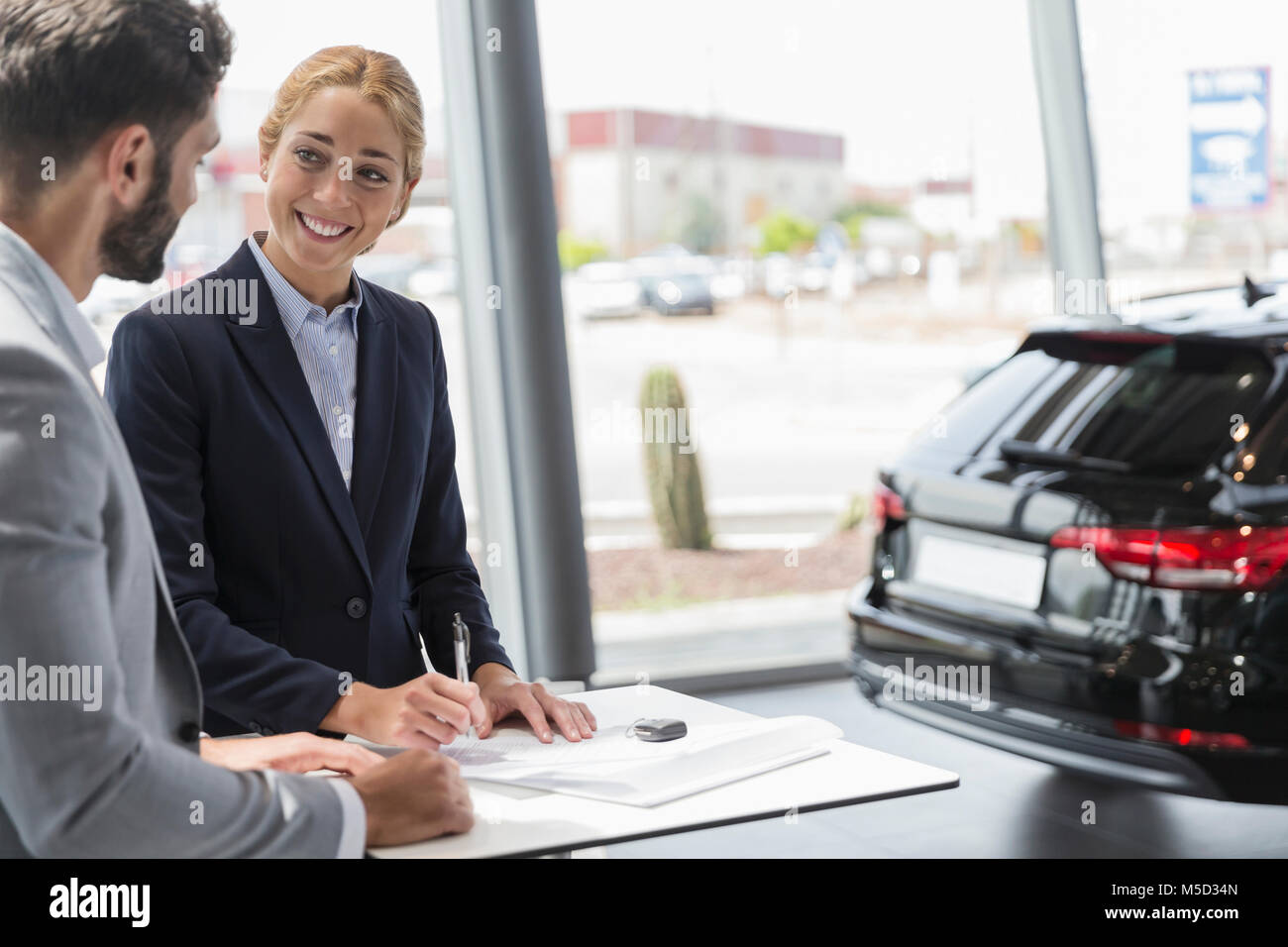 Car saleswoman and male customer signing contract paperwork in car dealership showroom Stock Photo