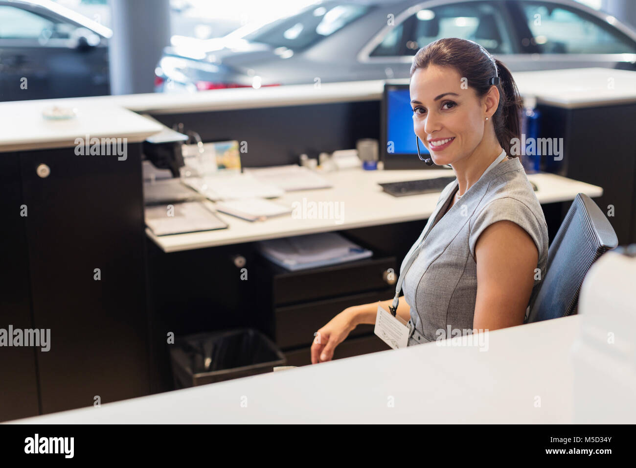 Portrait smiling, confident female receptionist working at desk in car dealership showroom Stock Photo