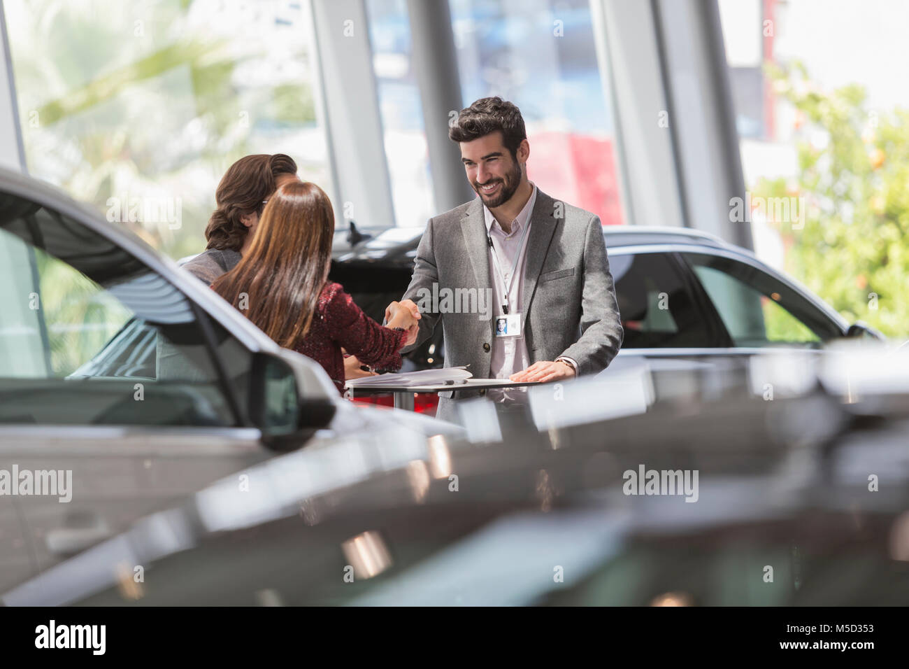 Car salesman handshaking with customers in car dealership showroom Stock Photo