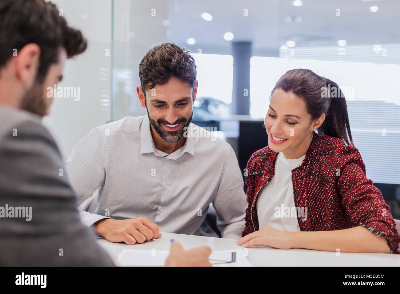 Car salesman explaining financial contract paperwork to couple customers in car dealership office Stock Photo