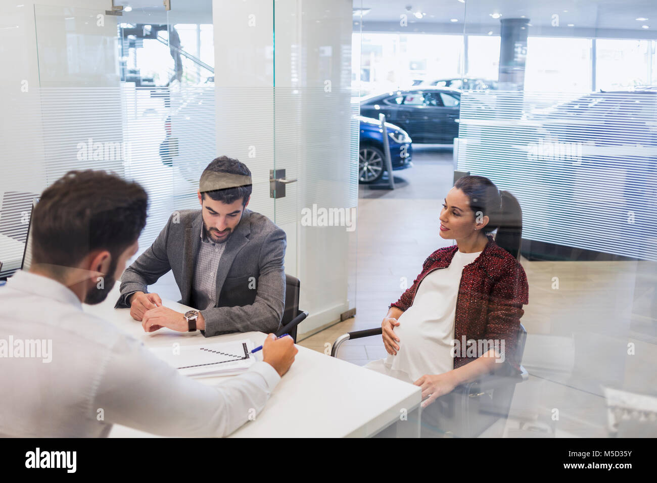 Car salesman explaining financial contract paperwork to pregnant couple customers in car dealership office Stock Photo