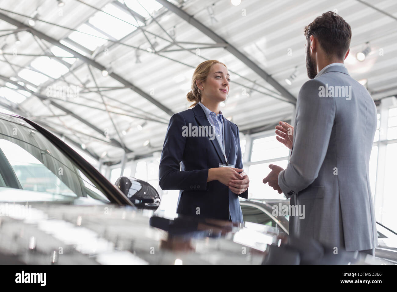 Car saleswoman talking to male customer in car dealership showroom Stock Photo