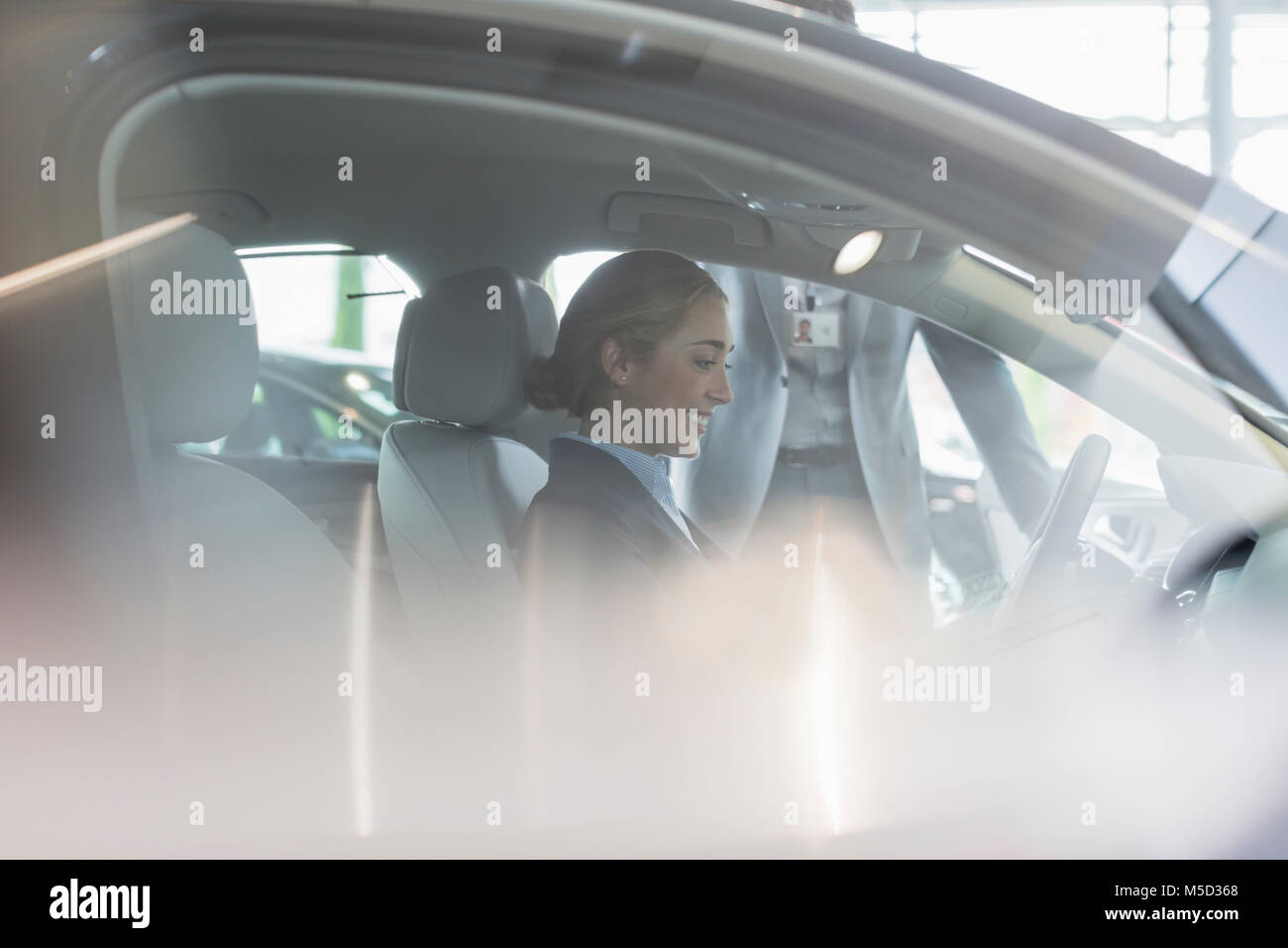 Smiling female customer sitting in driver’s seat of new car in car dealership Stock Photo