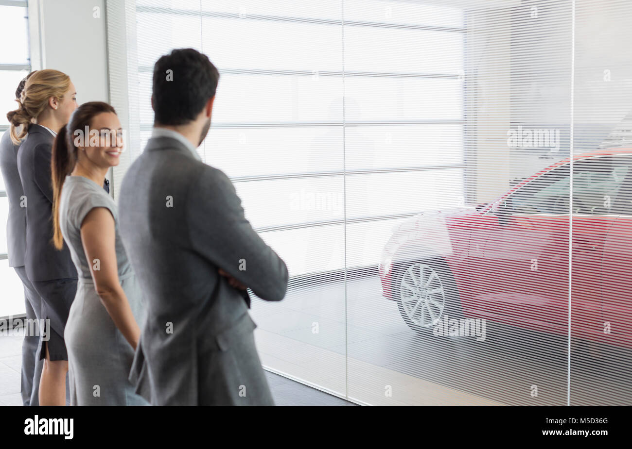 Car sales people looking at new, red car in car dealership showroom Stock Photo