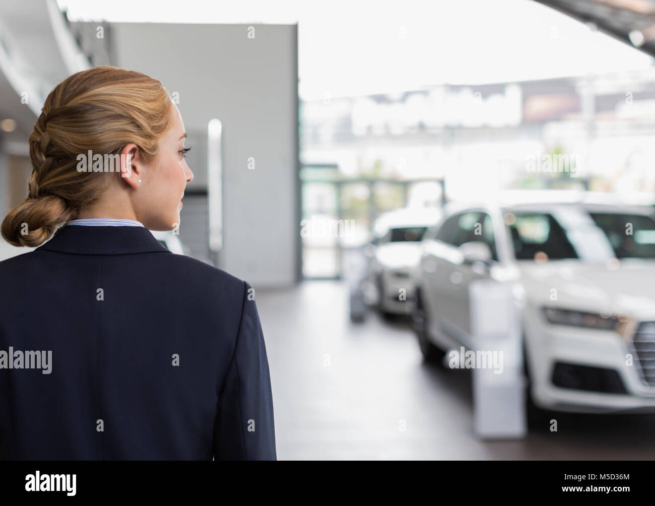 Blonde car saleswoman looking away in car dealership showroom Stock Photo