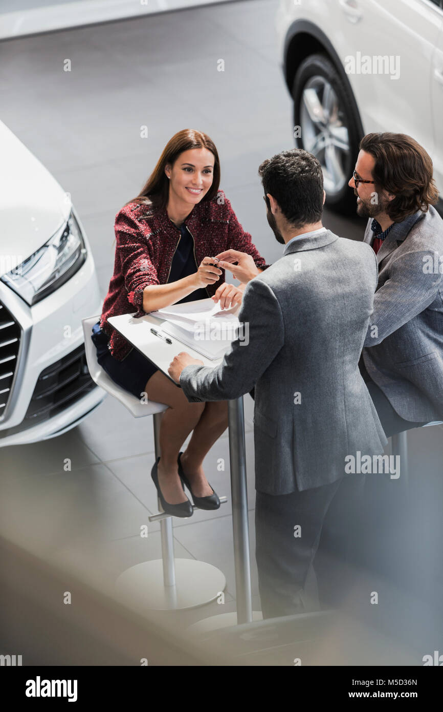 Car salesman giving car keys to smiling female customer in car dealership showroom Stock Photo