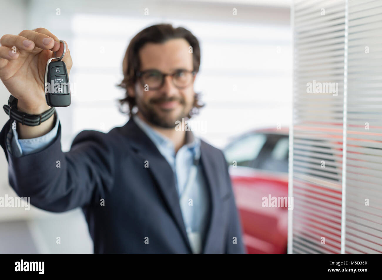 Portrait confident car salesman holding, showing car key in car dealership showroom Stock Photo
