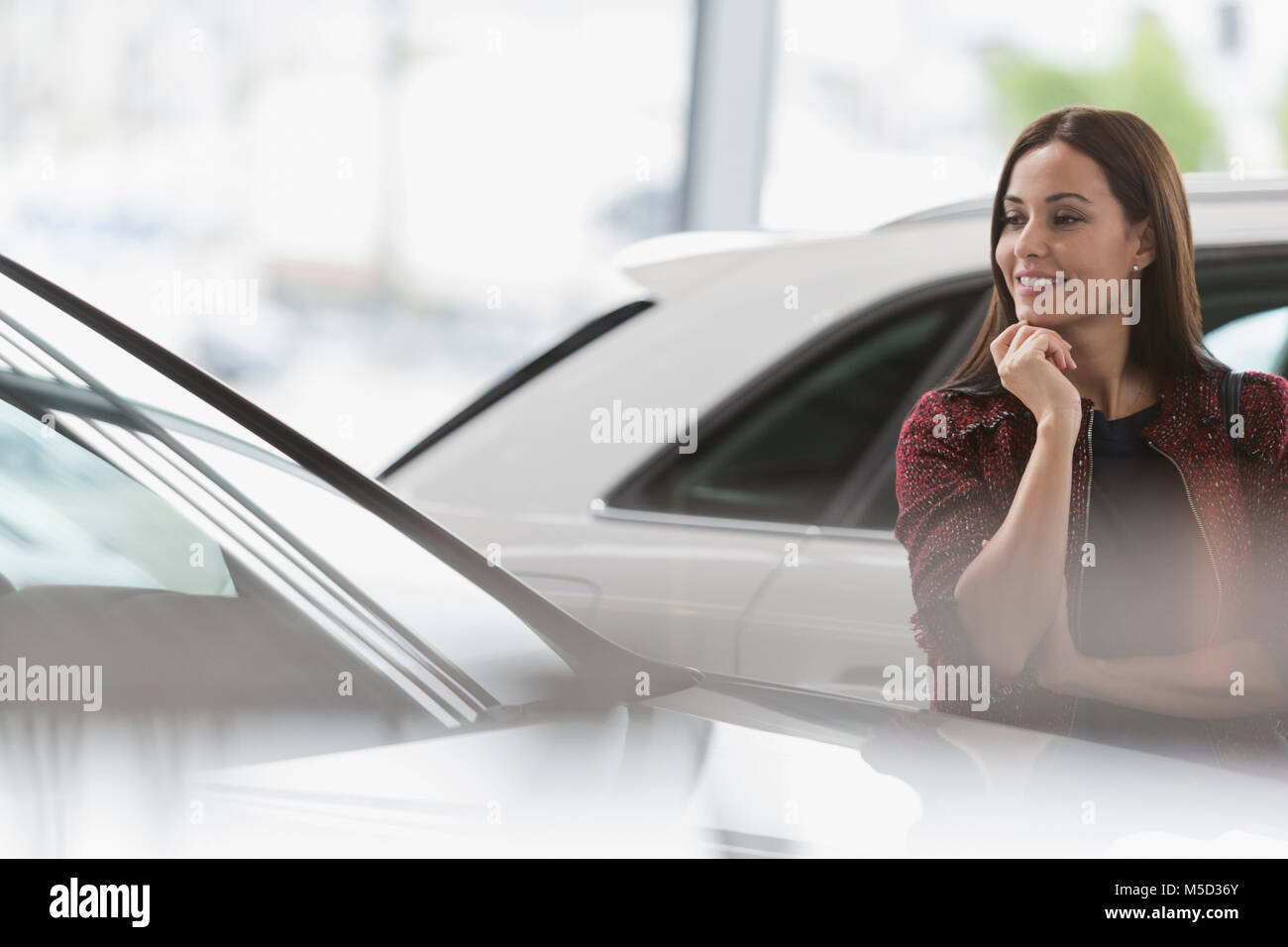 Smiling female customer eyeing new car in car dealership showroom Stock Photo