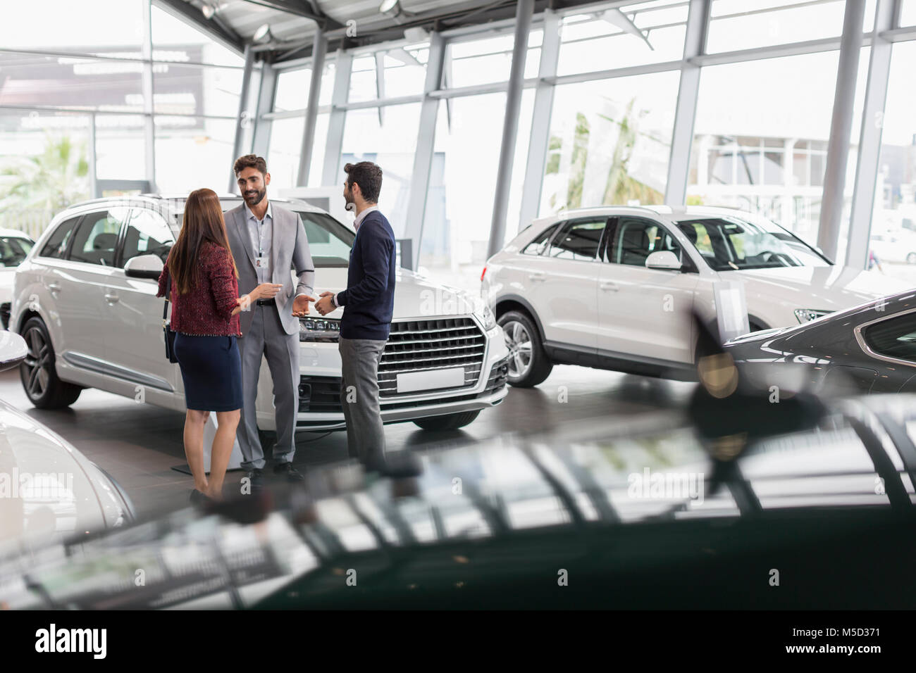 Car salesman talking to couple customers in car dealership showroom Stock Photo