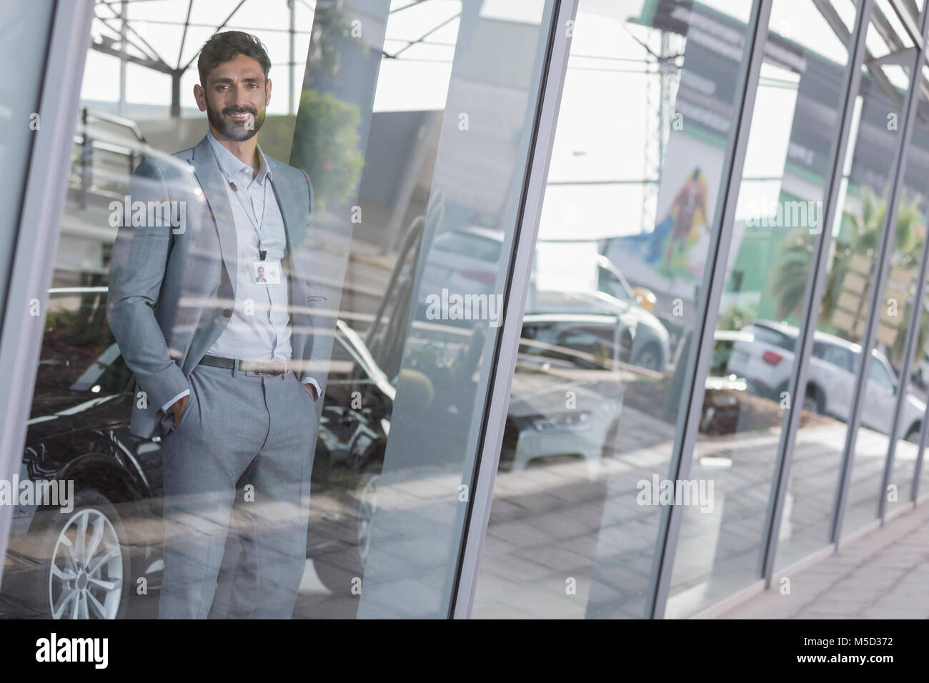 Portrait confident car salesman standing in window at car dealership showroom Stock Photo