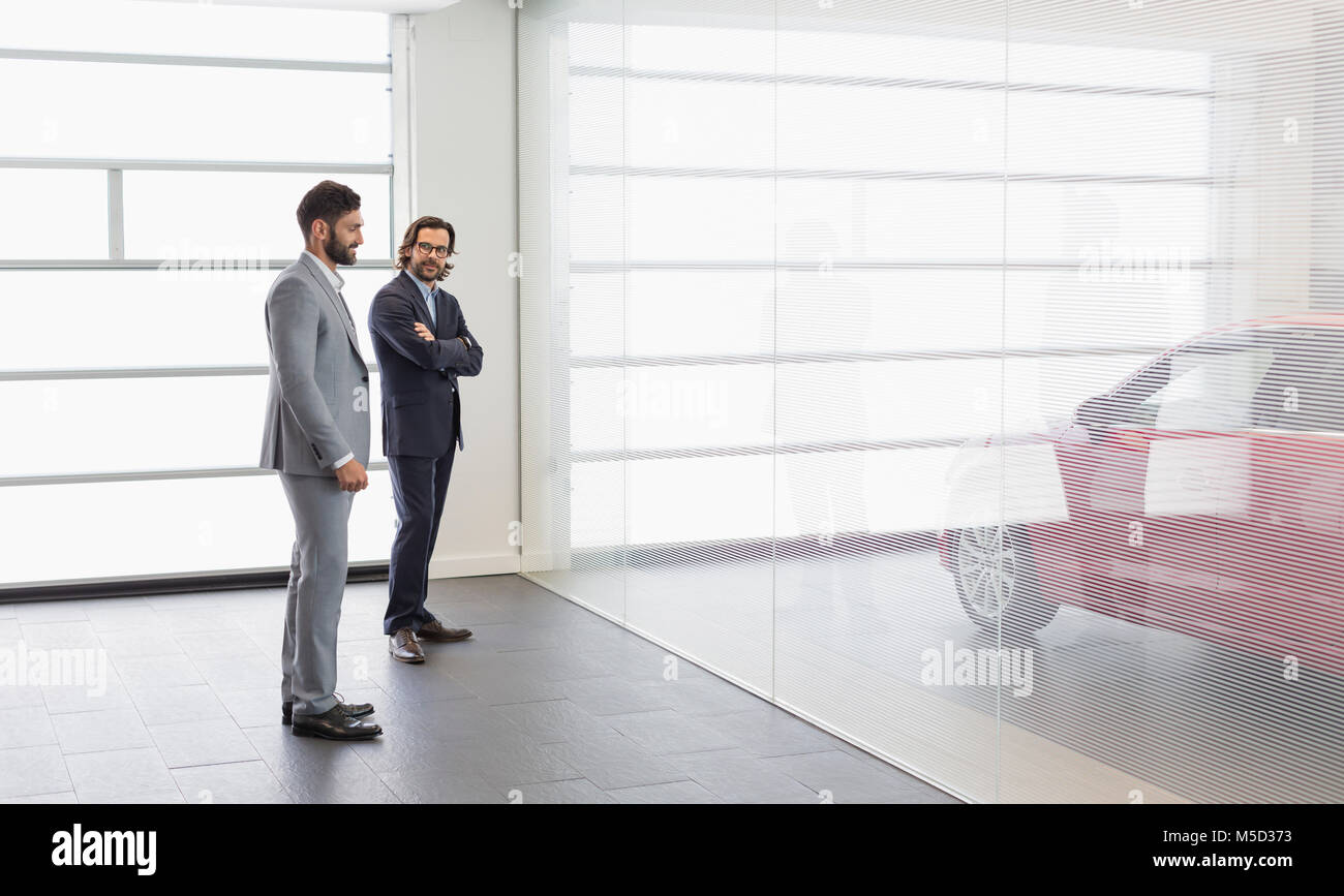 Car salesman and male customer looking at new car in car dealership showroom Stock Photo