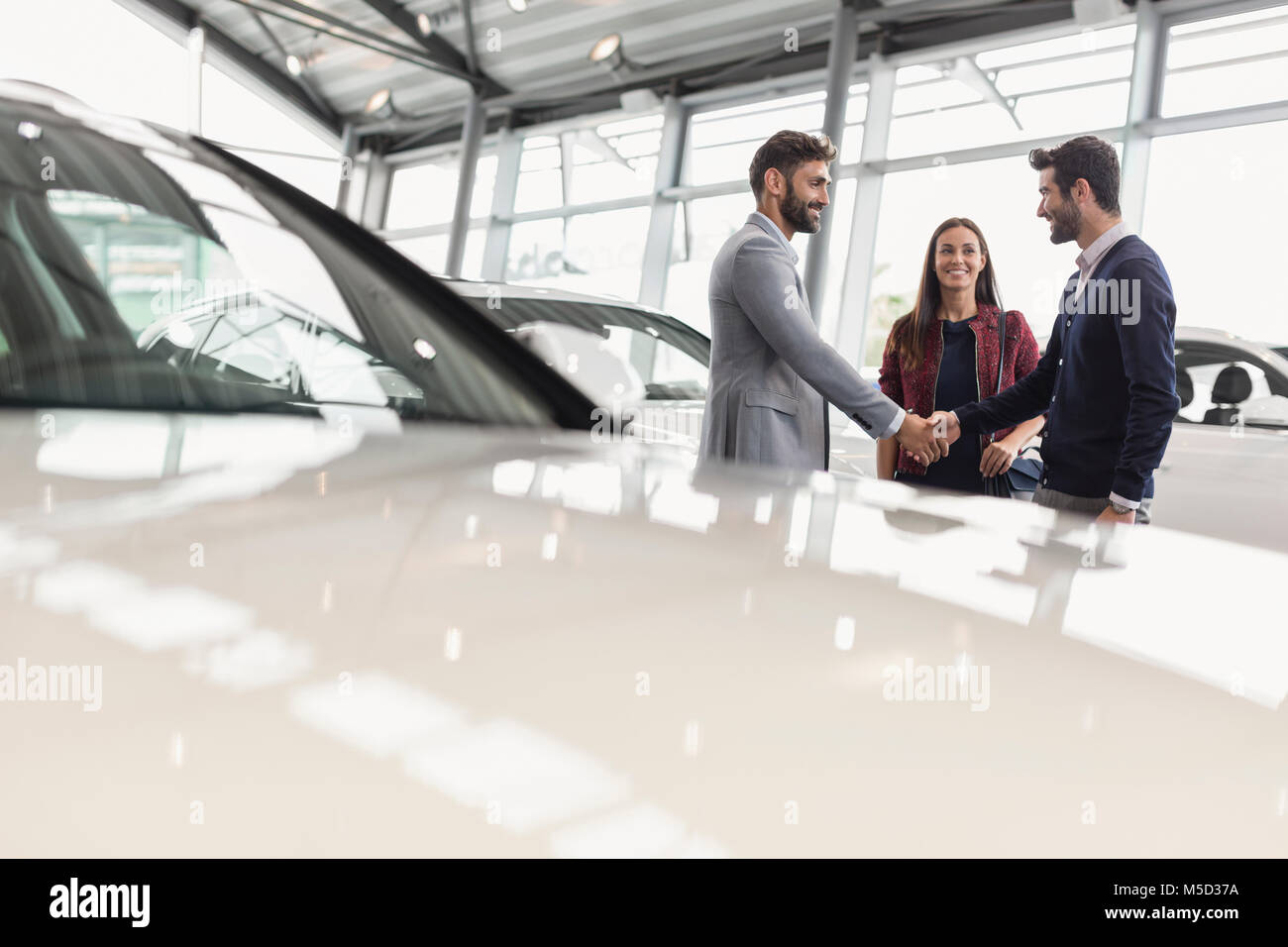 Car salesman shaking hands with couple customers in car dealership showroom Stock Photo