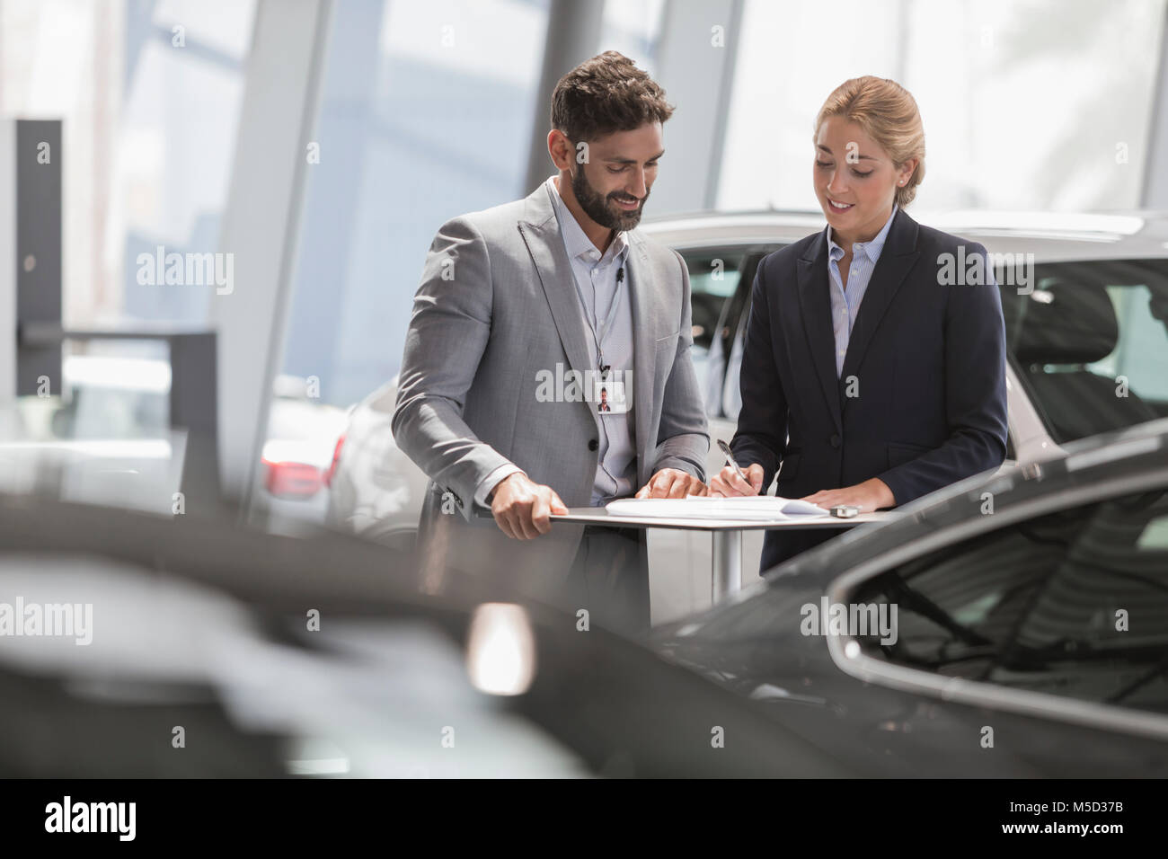 Car salesman and female customer reviewing financial contract paperwork in car dealership showroom Stock Photo