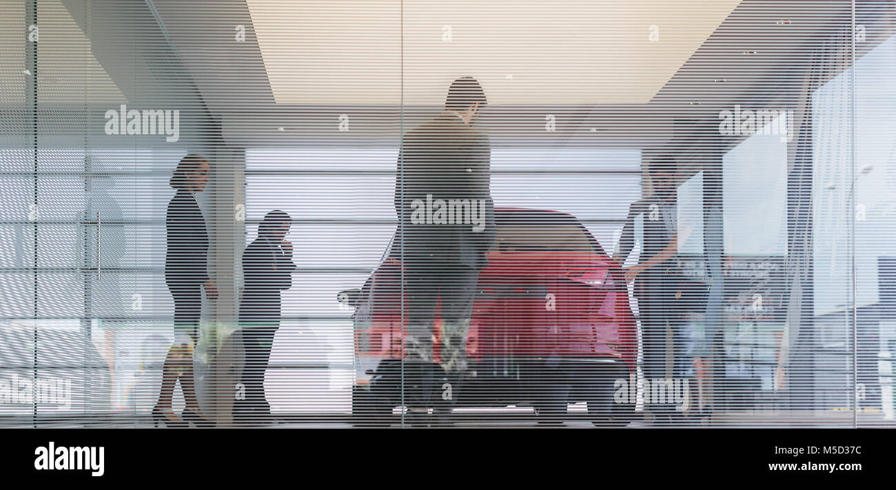 Car sales people and customers looking at new car in car dealership showroom Stock Photo
