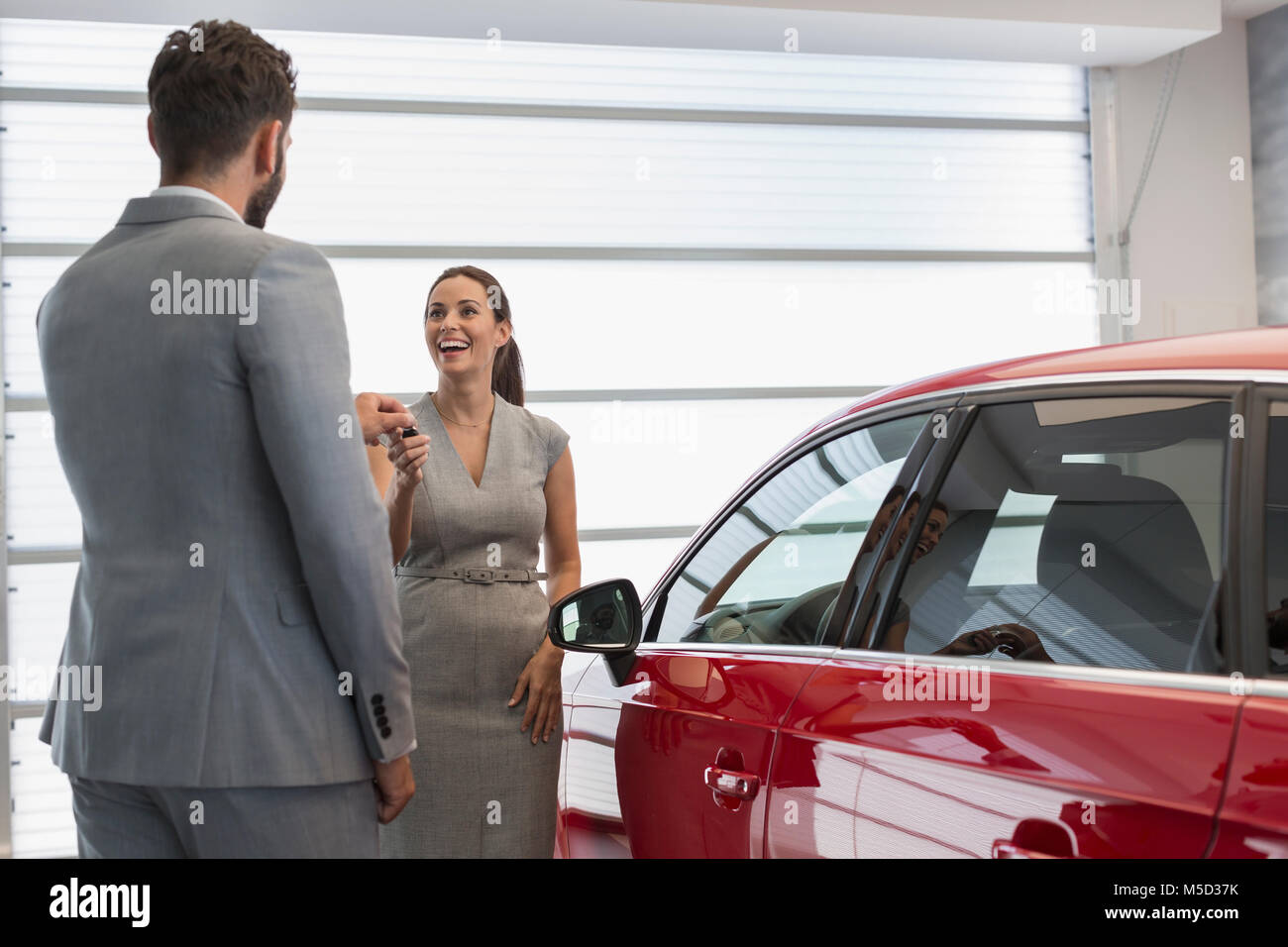 Car salesman giving keys to new car to female customer in car dealership Stock Photo