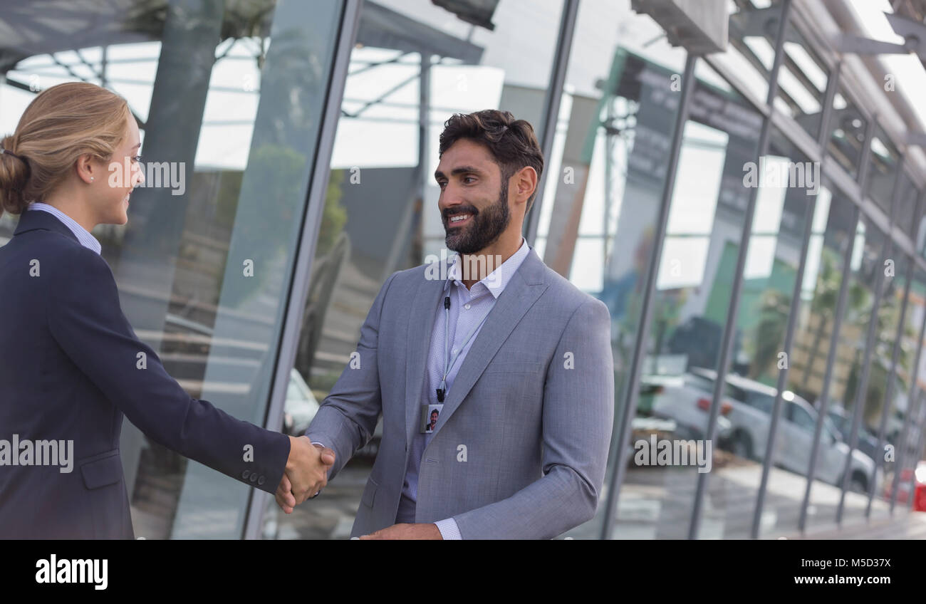 Car salesman greeting, shaking hands with female customer outside car dealership showroom Stock Photo
