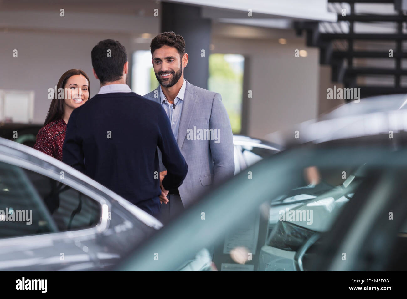 Car salesman greeting, shaking hands with couple customers in car dealership showroom Stock Photo