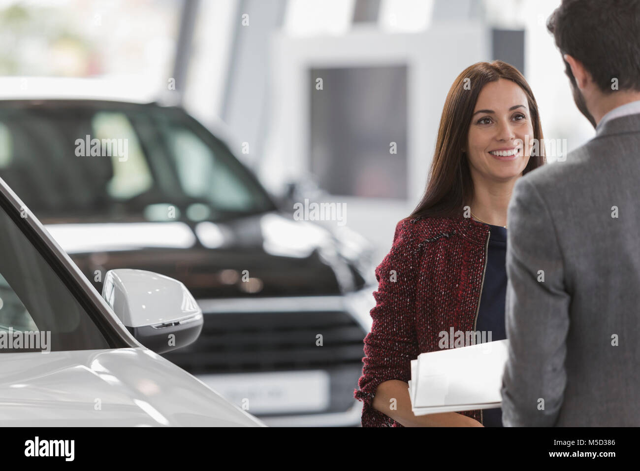 Smiling female customer listening to car salesman in car dealership showroom Stock Photo
