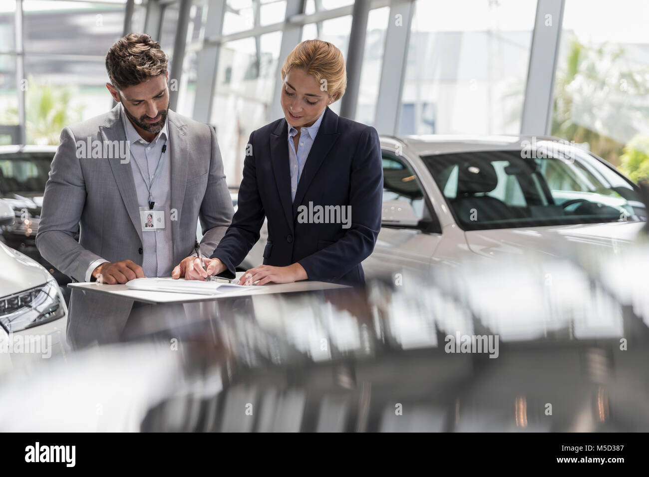 Car salesman watching female customer signing financial contract paperwork in car dealership showroom Stock Photo