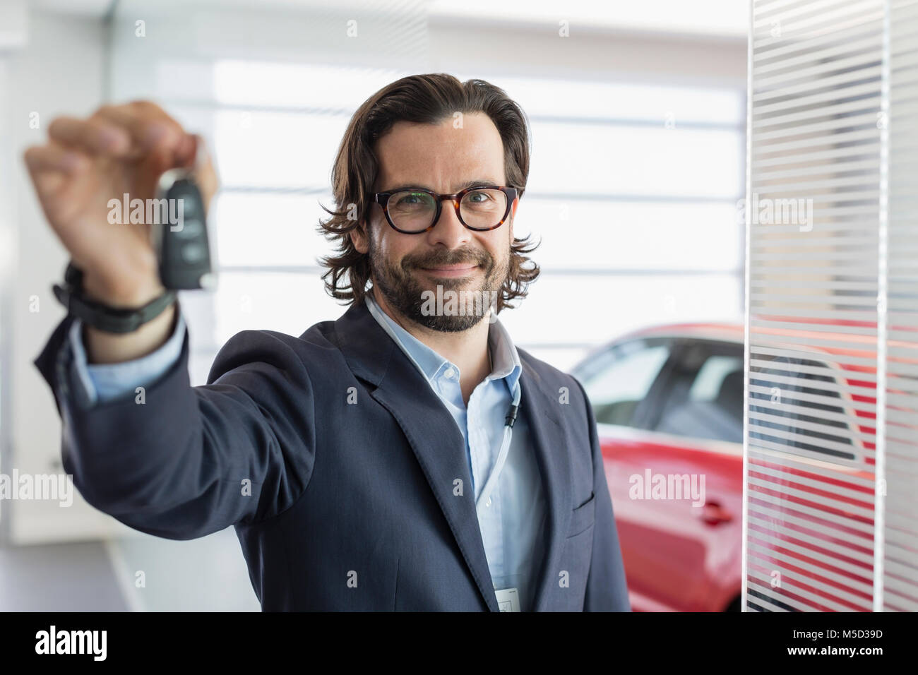 Portrait confident car salesman holding, showing car key in car dealership showroom Stock Photo