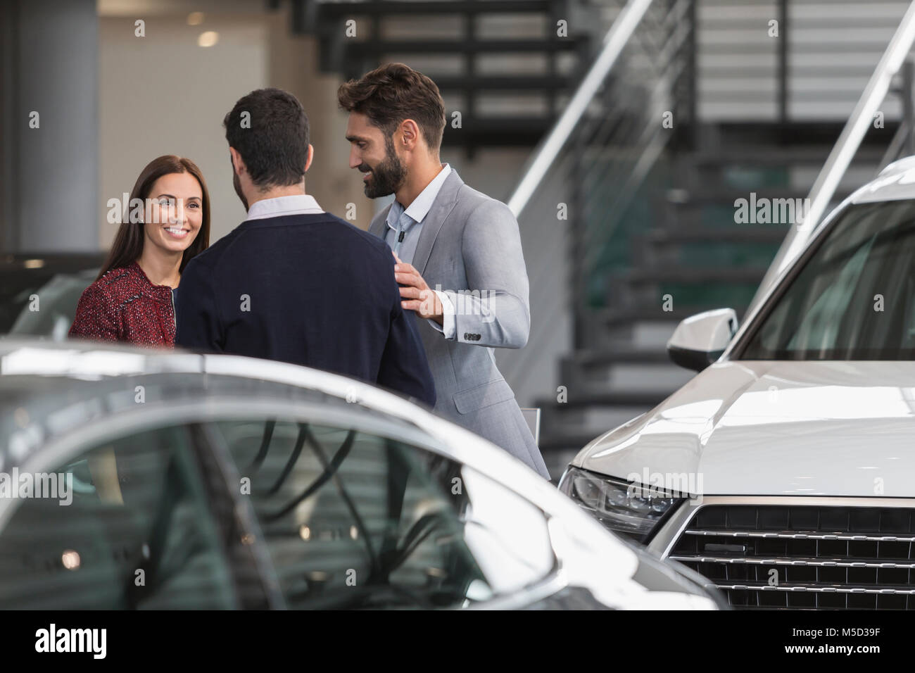 Car salesmen talking to female customer in car dealership showroom Stock Photo
