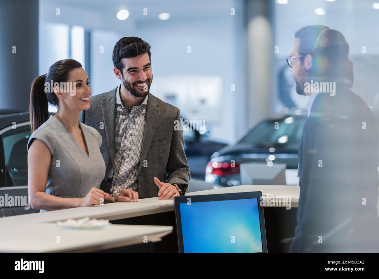 Couple customers talking to receptionist at desk in car dealership showroom Stock Photo