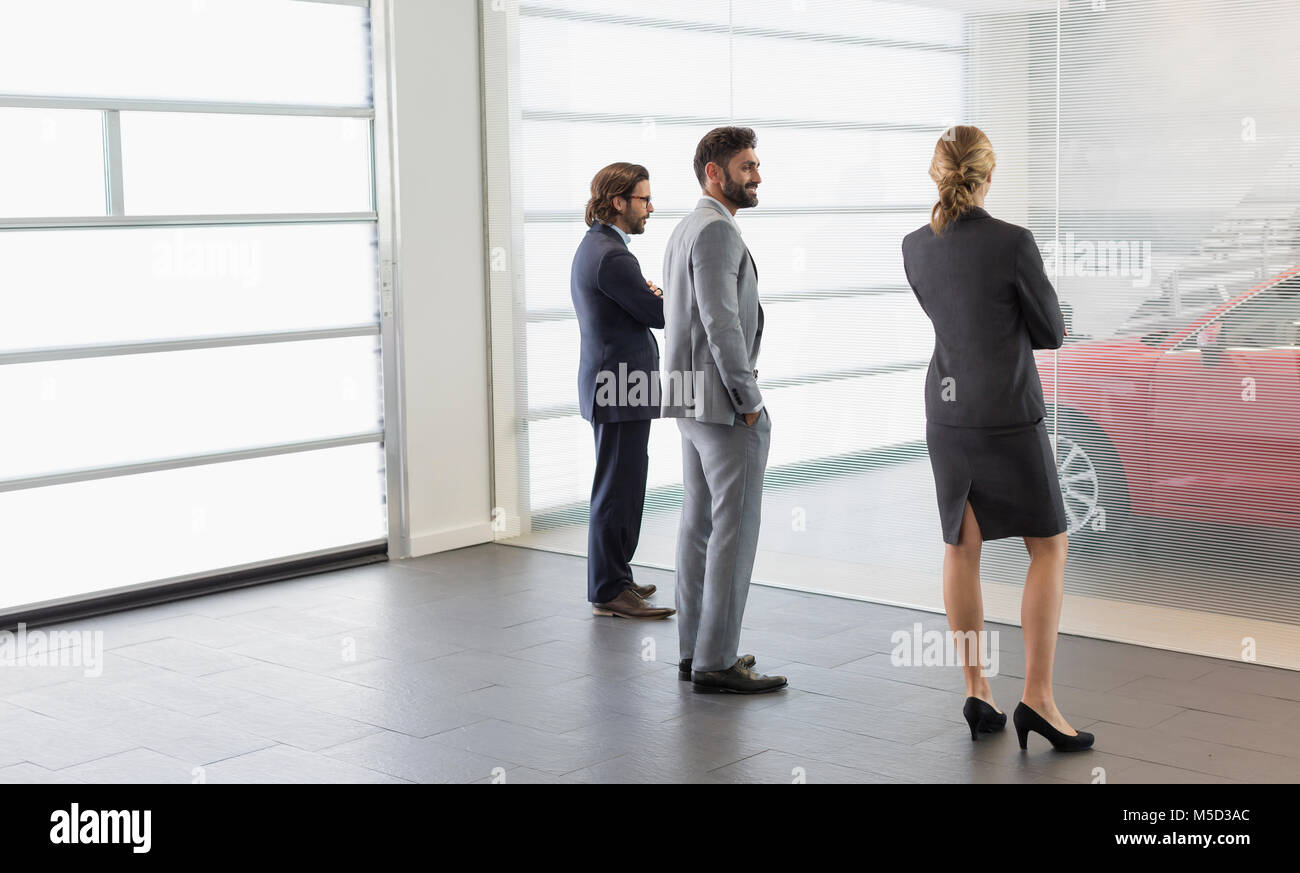 Car sales people and customer looking at new car in car dealership showroom Stock Photo