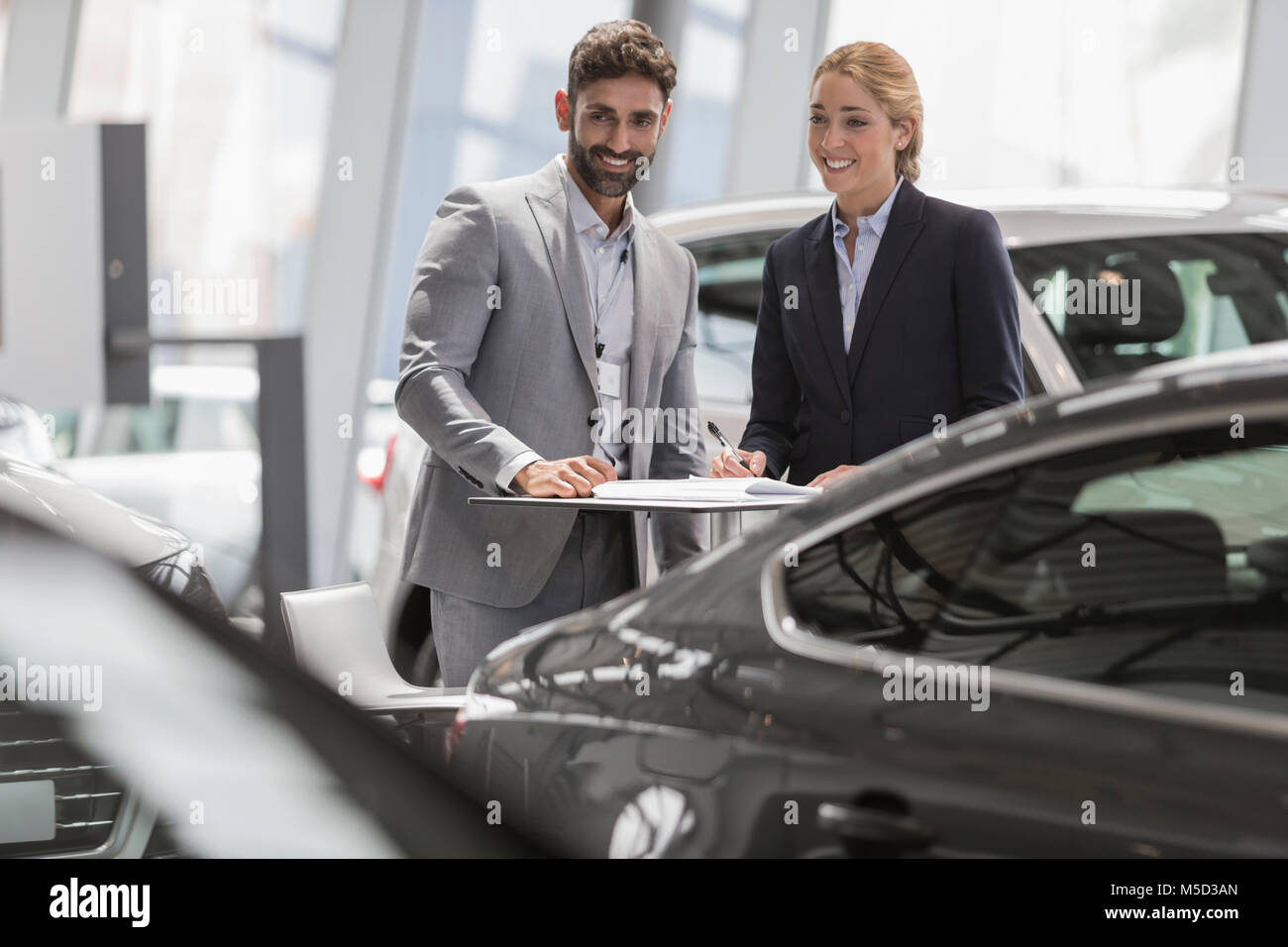 Car salesman and female customer looking at new cars in car dealership showroom Stock Photo
