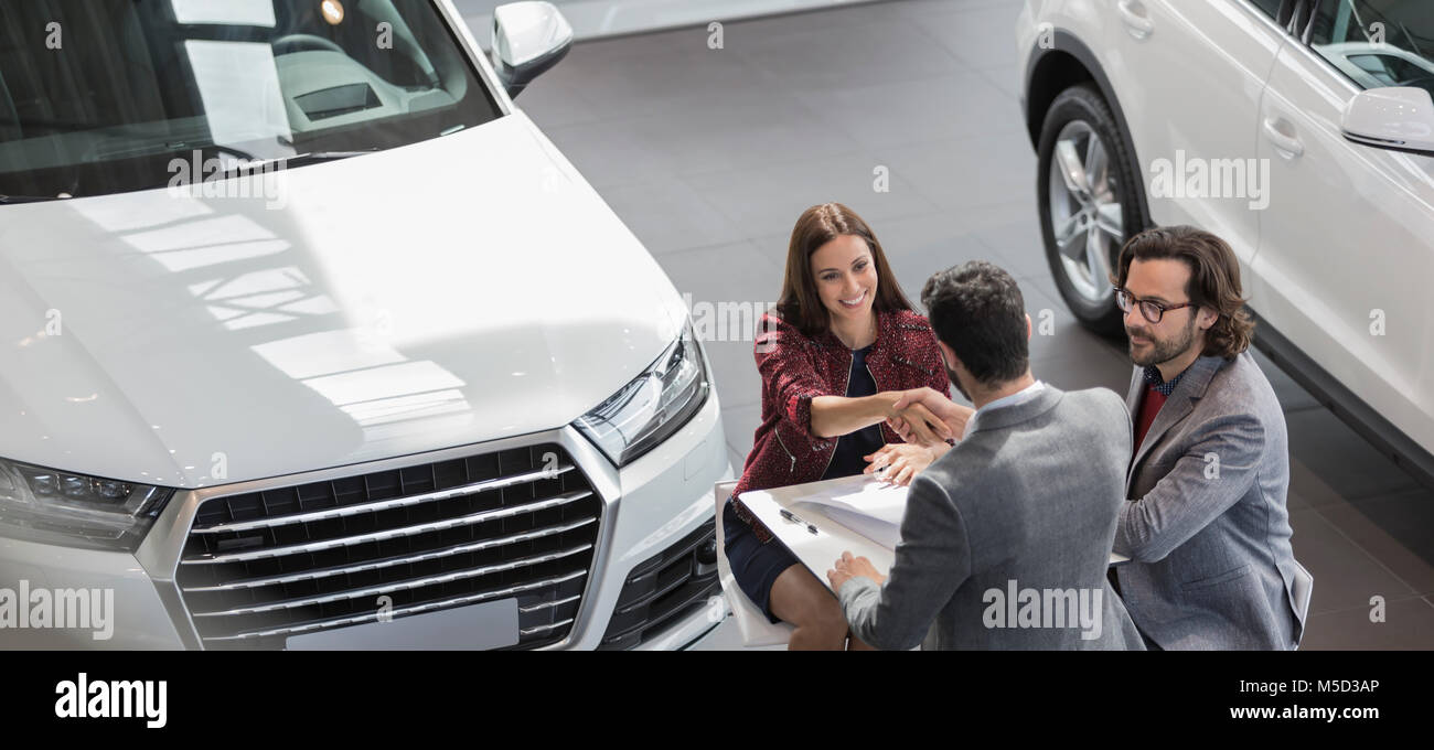 Car salesman shaking hands with female customer in car dealership showroom Stock Photo
