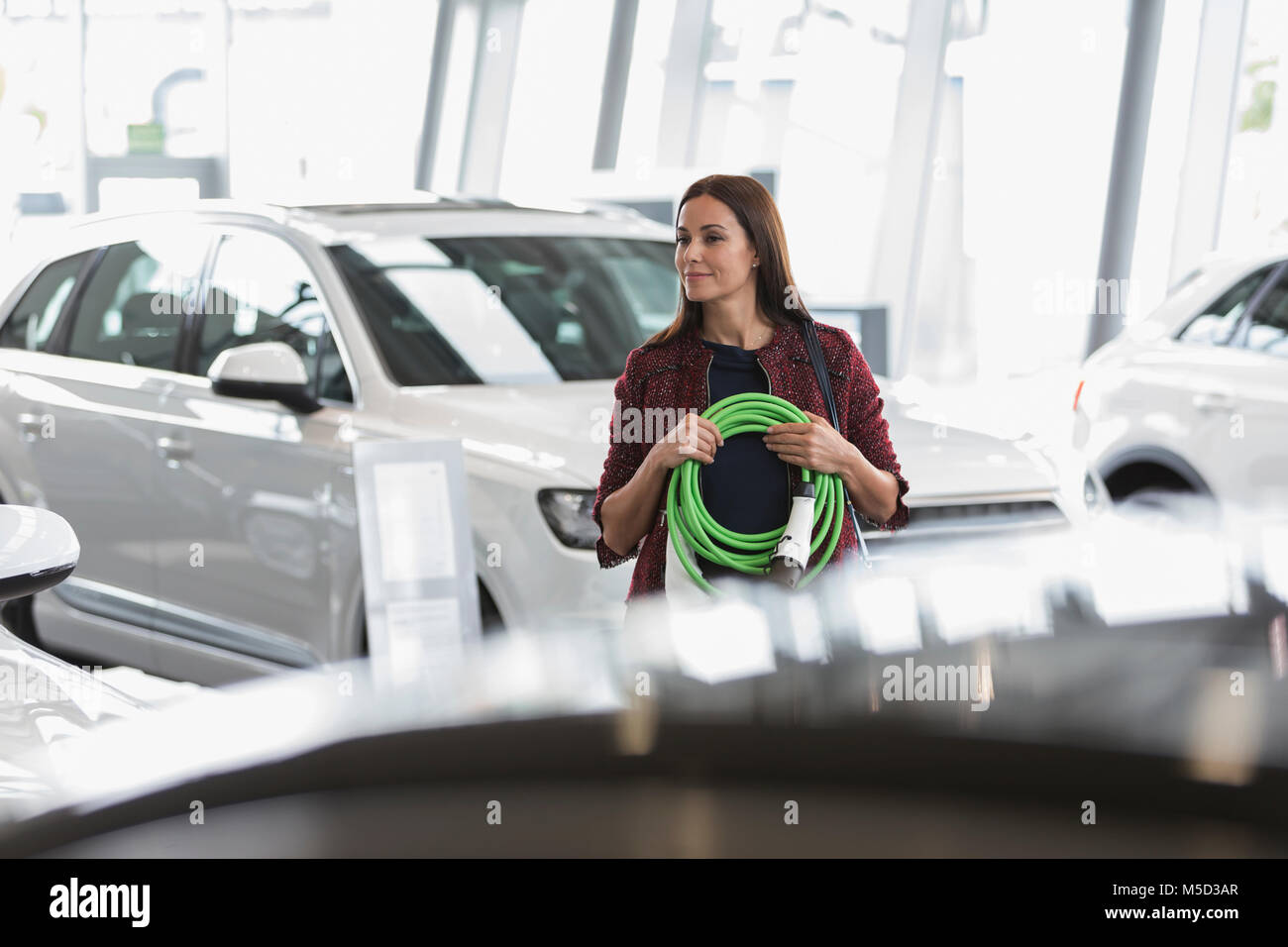 Female customer carrying hybrid charging cord in car dealership showroom Stock Photo