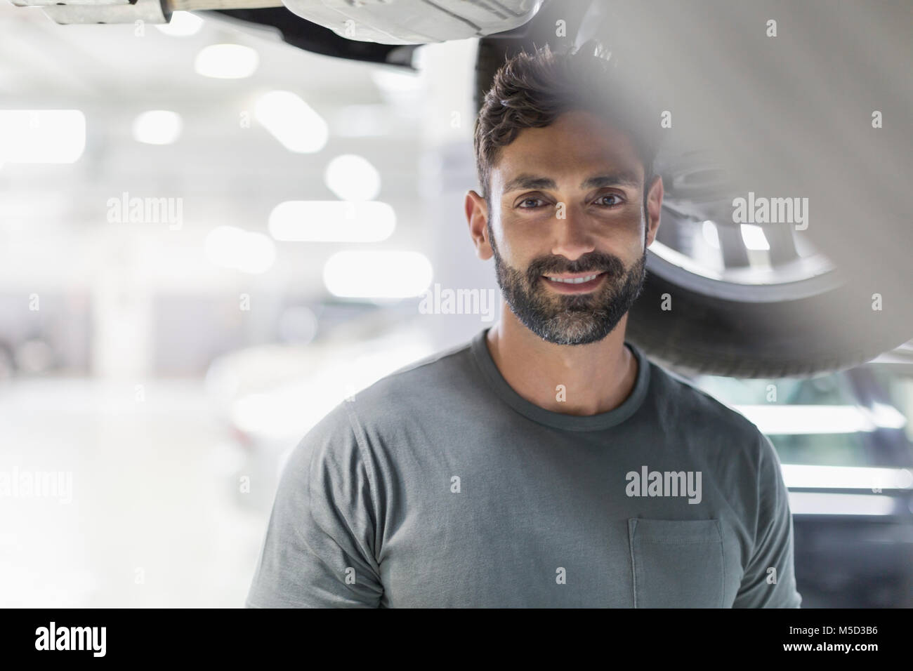 Portrait smiling, confident mechanic under car Stock Photo